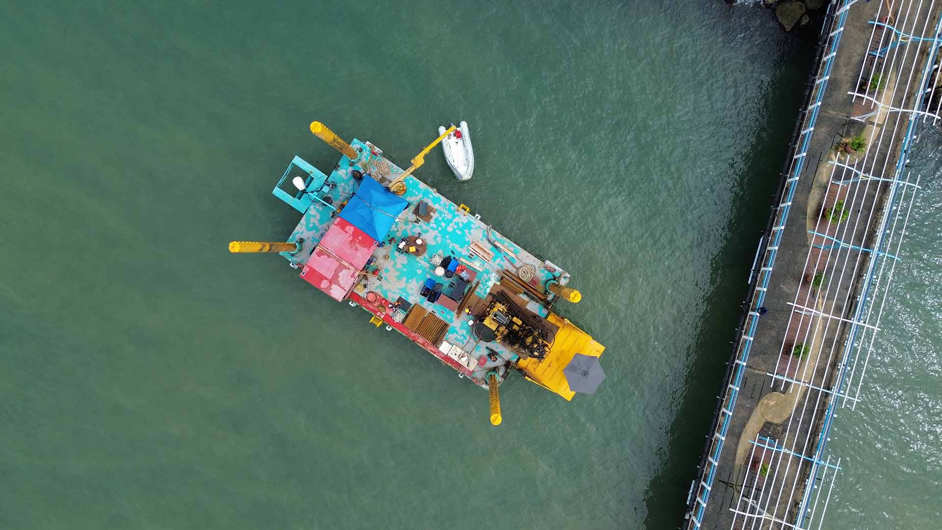 Aerial view of the barge used by Harbourside to conduct the marine-based drilling and geotechnical investigation. The pier of the cruise ship terminal can be seen on the right hand side, extending over vibrant tropical waters.